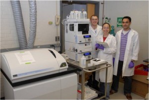 Bouwer group members in white lab coats stand next to the HPLC-ICP-MS in our lab.